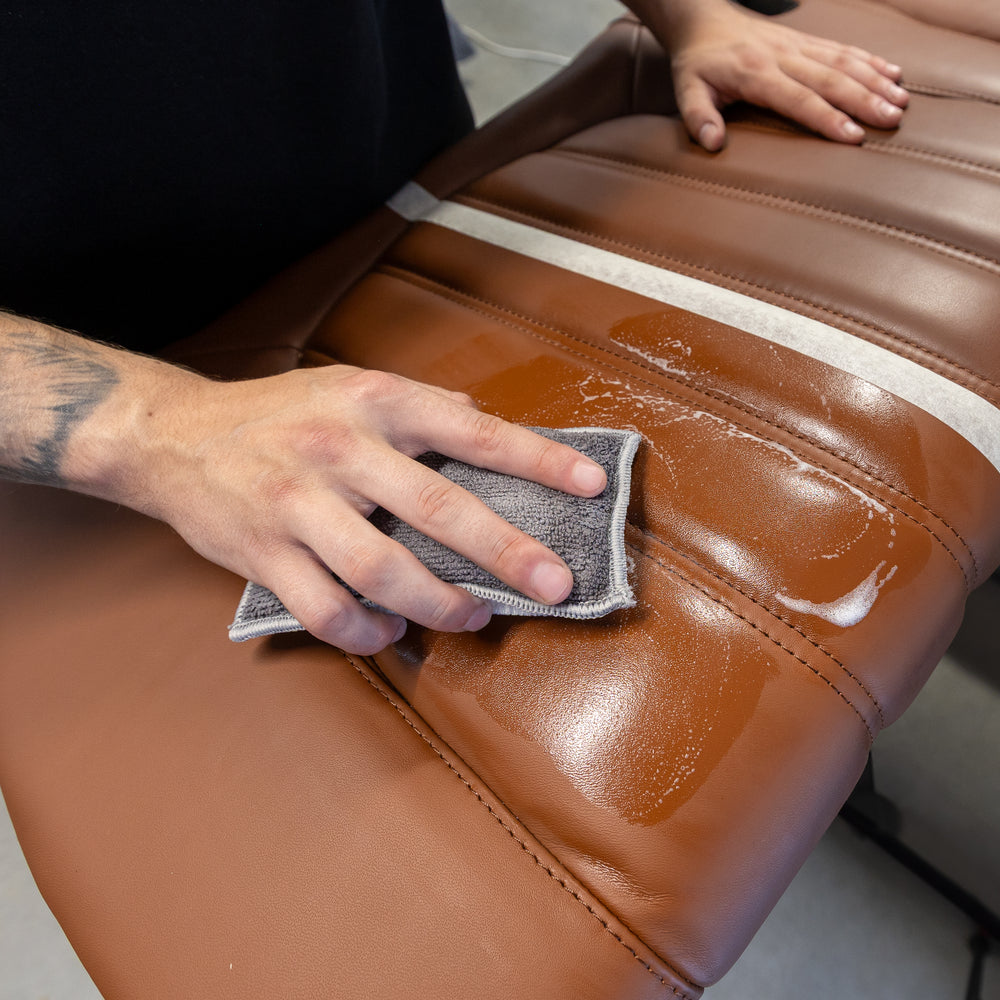 Leather Soft Cleaner wird mit einem Reinigungspad auf einem braunen Ledersitz verarbeitet